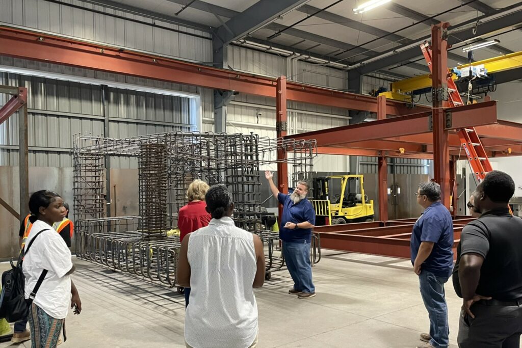 Several people are shown from behind, looking on as a guide explains rebar and iron beam setups.